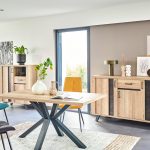 Photo d'une salle à manger avec une collection comprenant une enfilade, une table de repas, des chaises et un bibus. Les meubles présentent des finitions en chêne naturel style brut industriel et des piétements en métal noir.